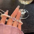 Detaillierte Makroaufnahme eines Perlenarmbands mit einem pinkfarbenen Herzanhänger. - Herz Rosa Stein Kunstperle Stil (35) / Weiß-Rosa
