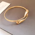 Detail view of a double-layered gold open bangle with teardrop ends on a textured gray background - Gold