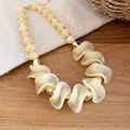 Detailopname van retro acrylaat ketting met onregelmatige crème kralen en gouden accenten - Ketting / Lichtkoffie
