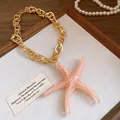 Macro view of a gold chain necklace with a large pink acrylic starfish pendant. - Starfish / Pink