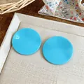 Detailed macro view of vibrant blue circular stud earrings on a textured cream tray - Blue