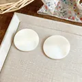 Detailed close-up of elegant white pleated round stud earrings on a display tray - White