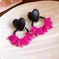 Close-up of retro heart wood earrings with pink shell fringe on a white textured plate. - Black and Rose Red