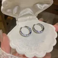 Detailed view of sparkling zircon hoop earrings inside a white shell jewelry box - Silver