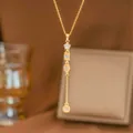 Detalle macro de un collar en forma de Y dorado con brillantes dijes de estrellas y geométricos - Estilo Largo Borla Geométrica (9495)