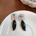 Close-up of acrylic floral drop earrings with black oval pendants on white plate - Blue Pink Black