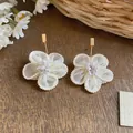 Primo piano di orecchini a fiore in tessuto bianco con dettagli in perle e perni quadrati dorati - Gancio per Orecchio Dorato (HE32493) / Bianco