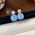 Detail view of geometric pearl stud earrings with iridescent blue square drops - Blue