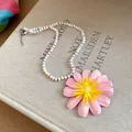 Top-down view of a pearl beaded necklace with a large pink flower pendant on a book. - Pink