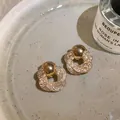 Dettaglio di orecchini a lobo a fiore in maglia dorata con perla metallica su un piatto. - Stud orecchini / Oro