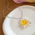 Close-up detail of a white daisy flower pendant on a pearl and clear bead necklace - White