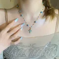 Detailed view of a vintage blue enameled cross necklace with stone beads on model - Blue