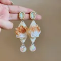 Detailed macro view of elegant resin rose dangle earrings with pearls and marble patterns - Gold-White