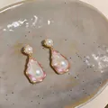Close-up of vintage irregular pearl earrings with pink enamel and gold wavy frame - Gold-White