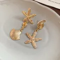 Detail view of gold-finished starfish and shell drop earrings on a ceramic tray - Silver Earring Post Style / Gold