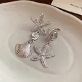 Detailed view of silver sea shell and starfish drop earrings with textured surface. - Silver Earring Post Style / Silver