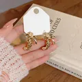 Detalle de elegantes pendientes dorados con nudo de lazo calado en una tarjeta de exhibición - Dorado