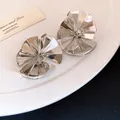 Detailed view of silver metallic ruffled flower stud earrings on white plate - Silver