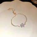 Close-up of elegant gold-toned bracelet featuring a sparkling zircon flower pendant. - Gold
