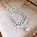 Detail view of a layered silver necklace with a frosted heart pendant and turquoise beads - Silver Chain with Blue & White Beads