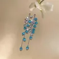 Detailed macro view of blue cat-eye stone tassel earrings with silver finish and zircons. - Blue