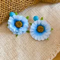 Detailweergave van handgemaakte lichtblauwe stoffen madeliefje oorbellen op mat. - Tops / Blauw
