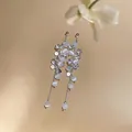 Close-up of silver-tone tassel earrings featuring zircon and white cat eye stone beads. - White