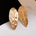 Detailed close-up view of oversized metallic gold leaf earrings with hammered texture - Gold