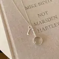 Detail view of silver necklace featuring magnifying glass and key charms on a vintage book. - Magnifying Glass & Key Dual Pendant / Silver