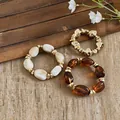 Detailansicht von drei klobigen Acryl-Stretch-Armbändern in Bernstein, Creme und Gold. - 3er-Set (S/M/L) / Kaffee und Khaki