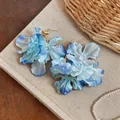 Close-up detail of layered blue gradient fabric flower earrings with gold studs. - Blue