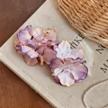 Close-up detail of purple and peach fabric flower earrings on a textured book - Pink