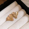 Close-up of gold-plated heart stud earrings with a hammered textured surface finish. - Stud Earrings / Gold