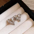 Macro view of silver metallic heart earrings with a textured molten surface in a tray. - Stud Earrings / Silver