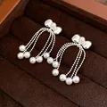 Detailed shot of silver bow earrings with multi-strand pearl tassels in a velvet box. - Bow Tassel / Silver