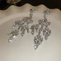 Close-up shot of sparkling rhinestone tassel heart earrings displayed on a wavy ceramic plate. - Clip-on Style (HE24853) / Silver-Pink