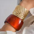 Detailed macro view of wide amber resin bangle and gold textured feather cuff bracelet. - Gold + Coffee