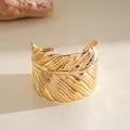 Detailed view of the intricate gold feather texture on a wide metal cuff bracelet jewelry - Gold
