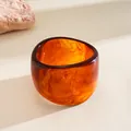 Macro view of wide irregular geometric resin bangle with amber texture - Brown