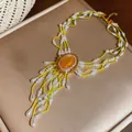Detailansicht einer mehrlagigen Perlenkette mit orangefarbenem Stein und Fransen - Grün/Weiß