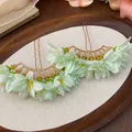 Macro view of elegant light green fabric flower hairpins with golden metal finish and water droplets - Green