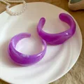 Dettaglio di due eleganti bracciali rigidi in resina viola marmorizzata su un piatto bianco. - Viola