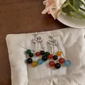 Primo piano di orecchini a nappa con perline di agata colorata su un cuscino crema - Colorato