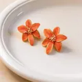 Dettaglio di eleganti orecchini a lobo a fiore arancione con bordi dorati su piatto bianco - Arancione