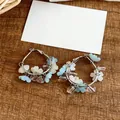 Macro detail of silver hoop earrings featuring blue and white resin flower charms - Blue