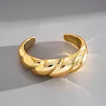 Primo piano di un bracciale rigido dorato lucido a spirale su uno sfondo neutro - Stile Metallo Intrecciato / Oro