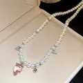 Close-up of pearl necklace with pink strawberry and heart charms in a beige jewelry box - Pink