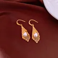 Elegant close-up view of golden lattice lace-work earrings with teardrop pearls on silk - Gold