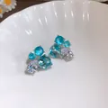 Gros plan de boucles d'oreilles géométriques en zircon bleu et clair dans un bol blanc - Bleu
