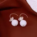 Detailed view of white textured bead earrings with silver floral hooks on dark brown fabric - Hook Style / Silver-White